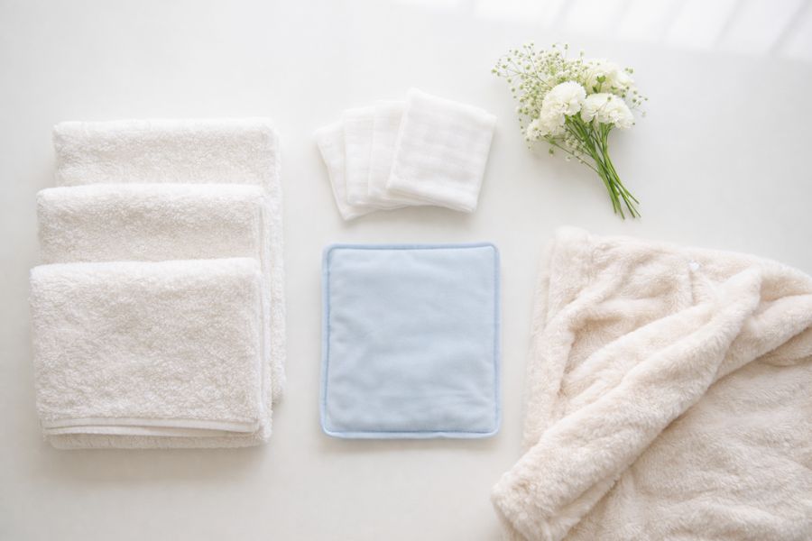 白いテーブルに並べられたタオルとガーゼと保冷剤と白いカーネーションのエンゼルケア用品一式