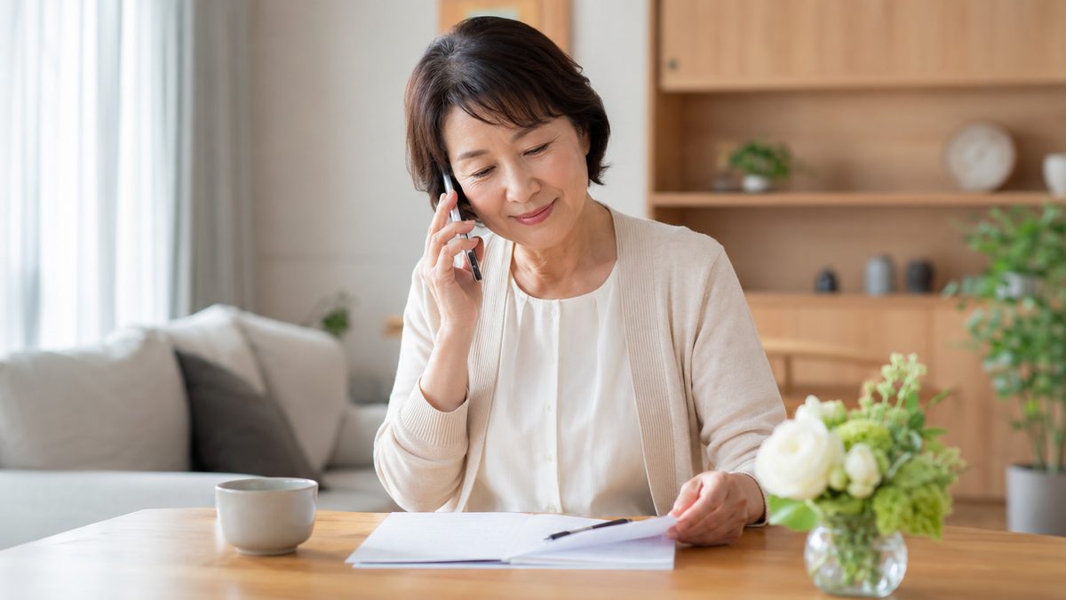 自宅で電話をしながらメモを取り穏やかに相談する女性