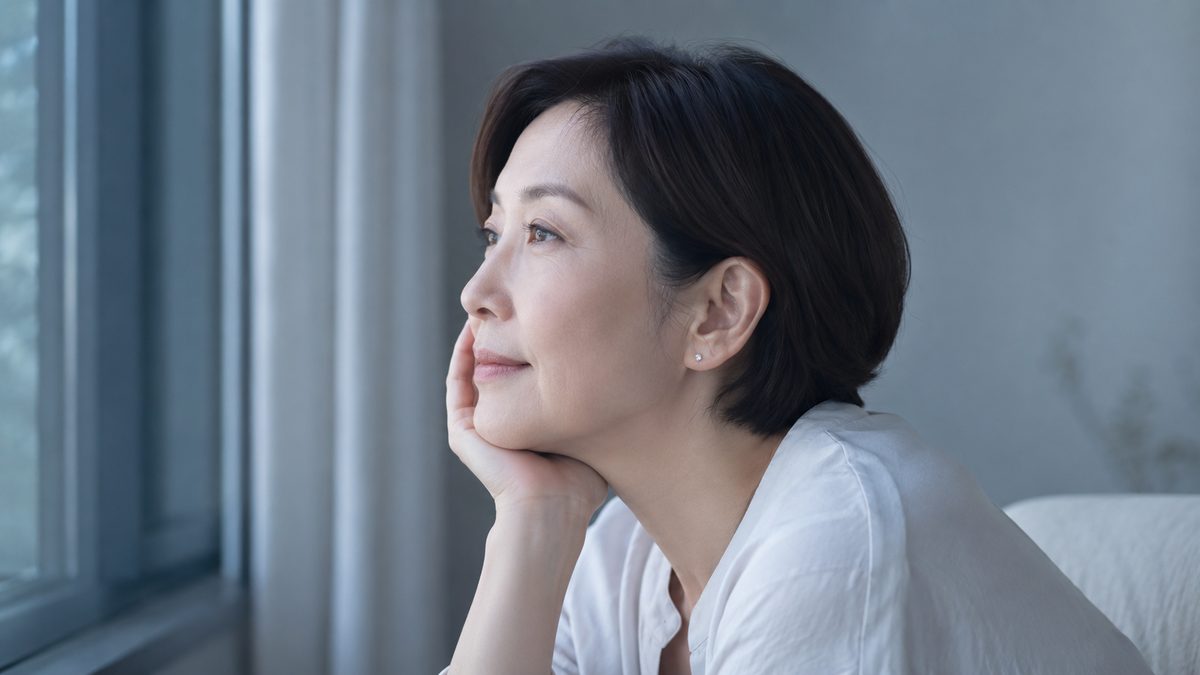 窓辺で頬杖をつき静かに外を眺める落ち着いた表情の女性