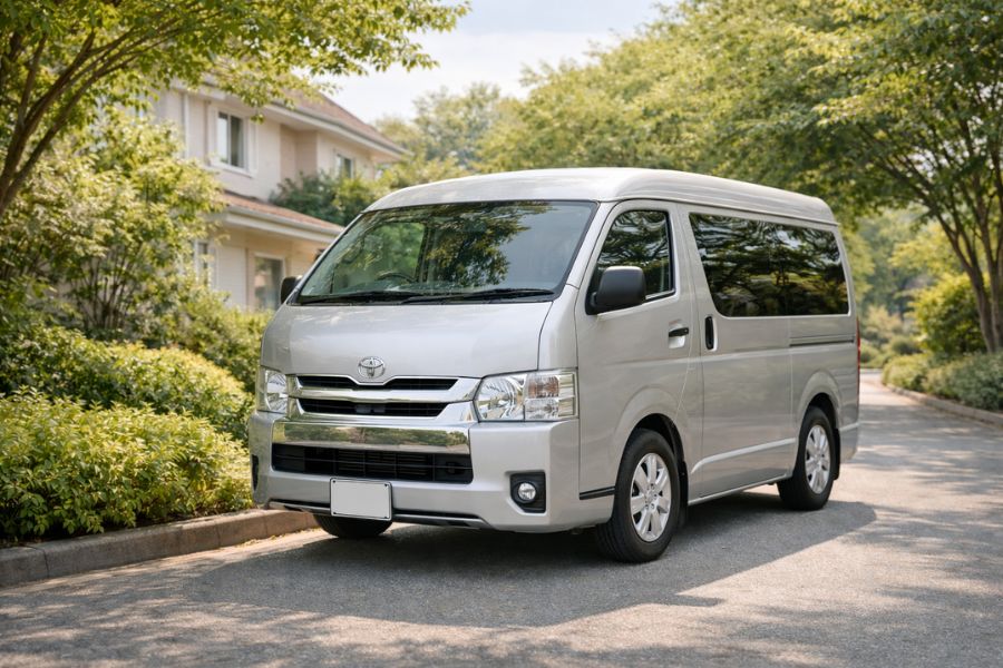 緑の木々が背景に広がる閑静な住宅街に停車した白い小型バン（移動火葬車）の外観
