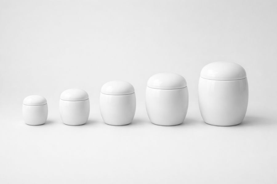 薄いグレー背景に白い陶器の骨壺が小さい順から大きい順まで五点一直線に並んだ商品撮影